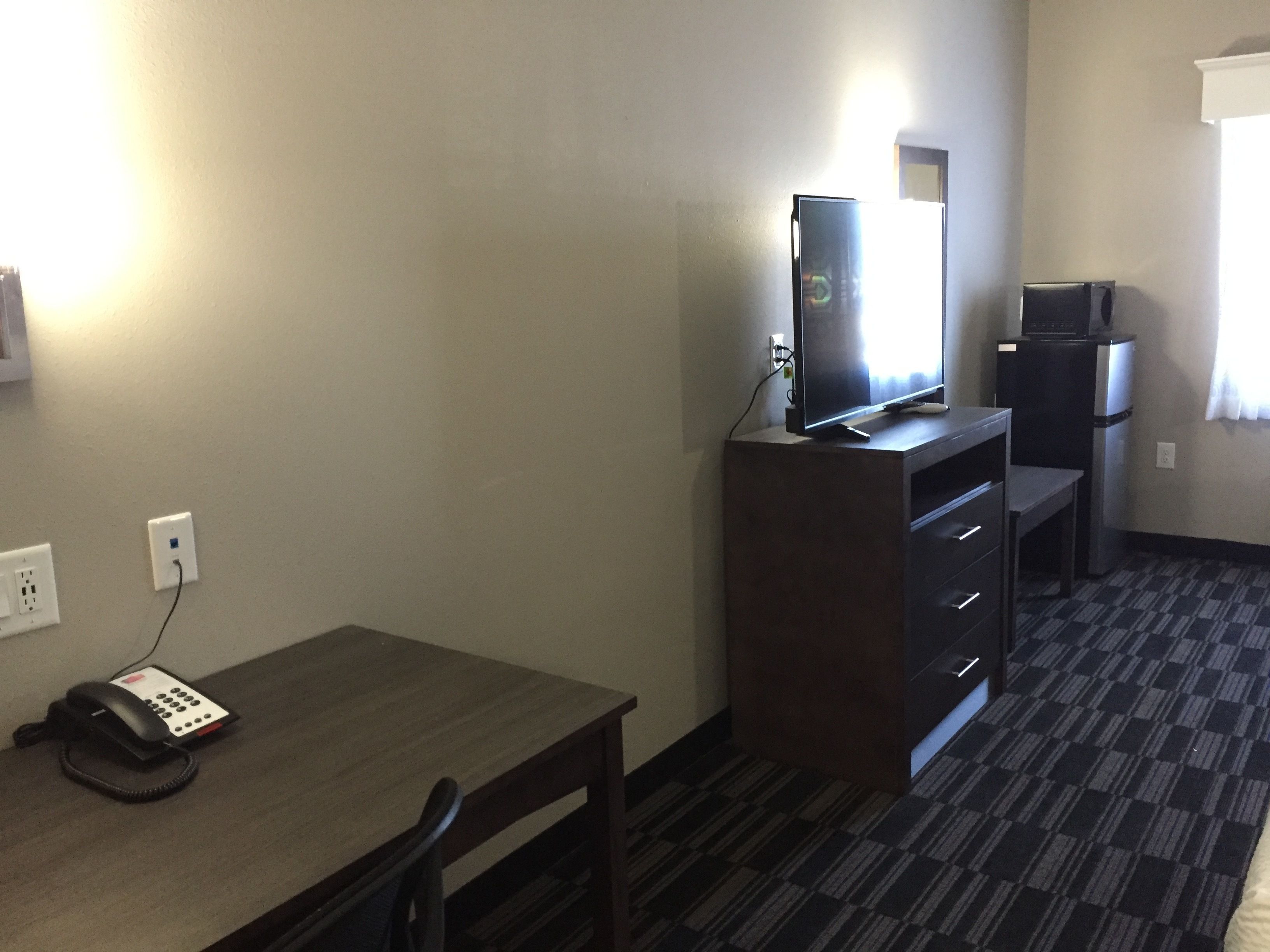 Een hotelkamer met een bureau, een computer, een koelkast en een telefoon.