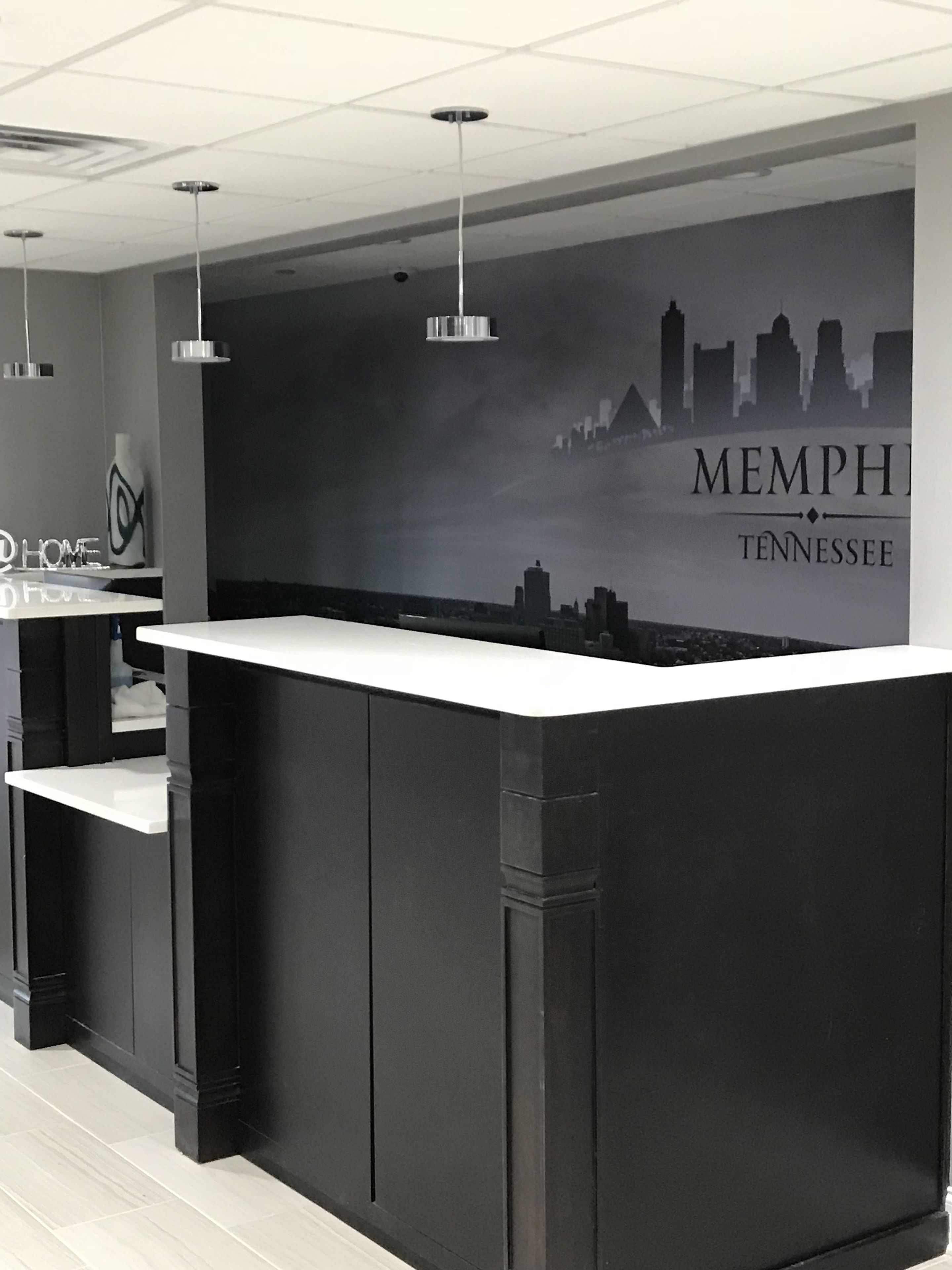 A modern reception desk with a cityscape mural in the background, a white countertop, and pendant lighting.