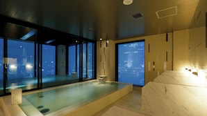 A modern spa area with a large bathtub, a view of the city at night, and a reception desk. - Candeo Hotels Tokyo Roppongi (Tokyo)