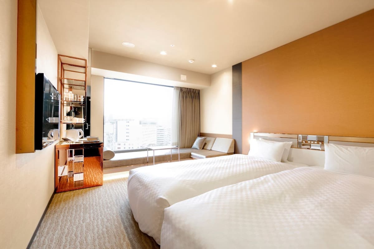 A hotel room with two beds, a seating area with a view, and a minibar.