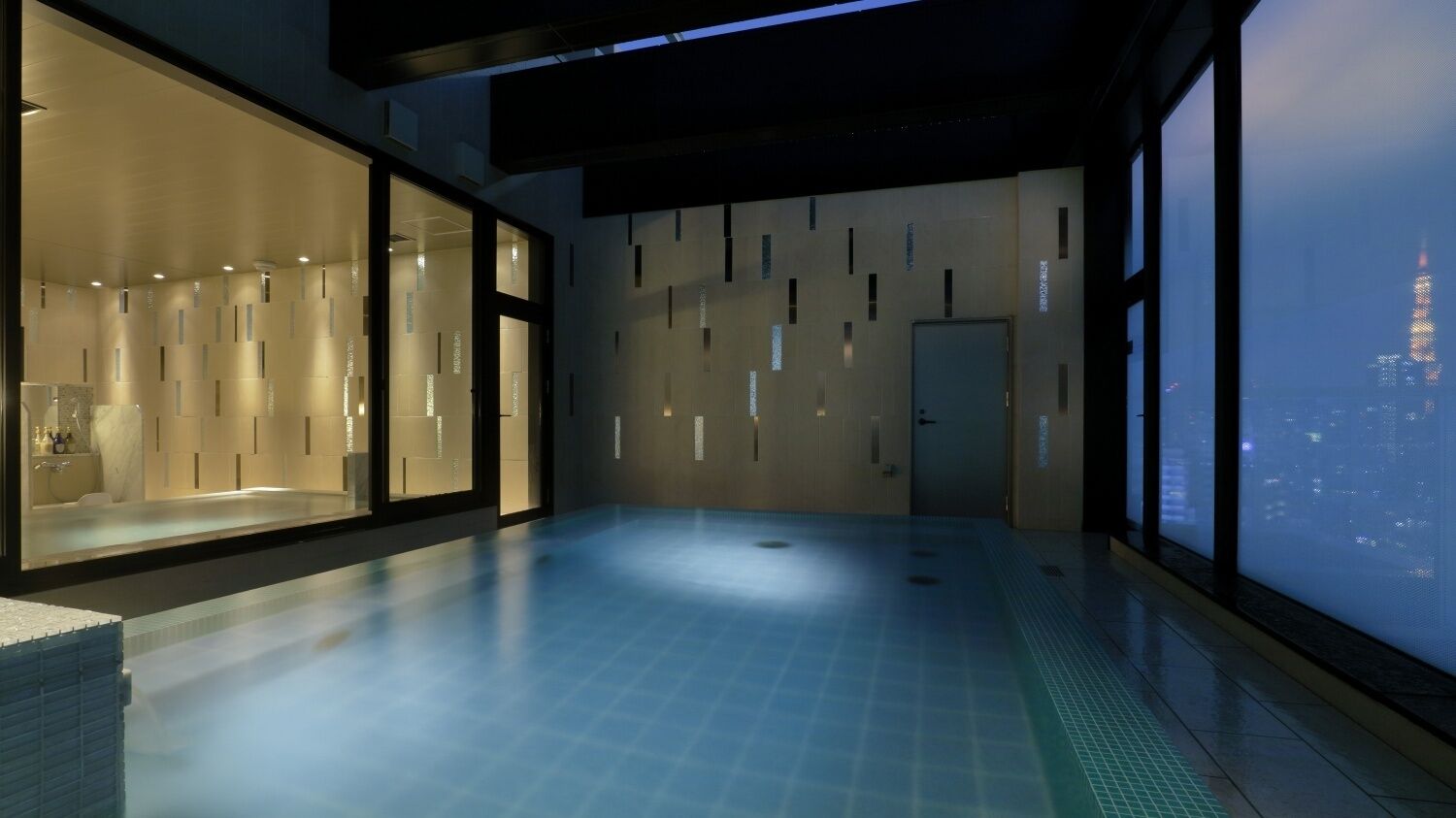 A modern hotel room with a large window overlooking a cityscape, a spacious interior, and a visible bathroom area.