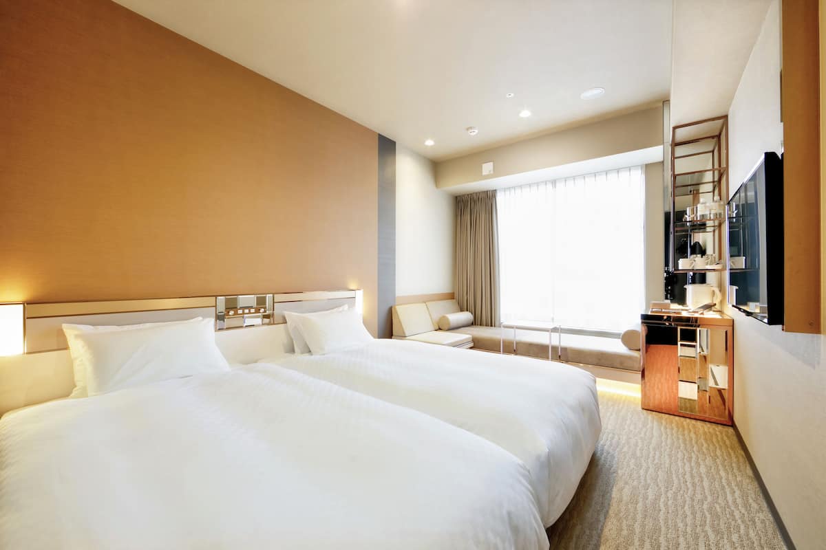 A hotel room with two large beds, a small seating area, a desk with a mirror, and a large window with curtains.