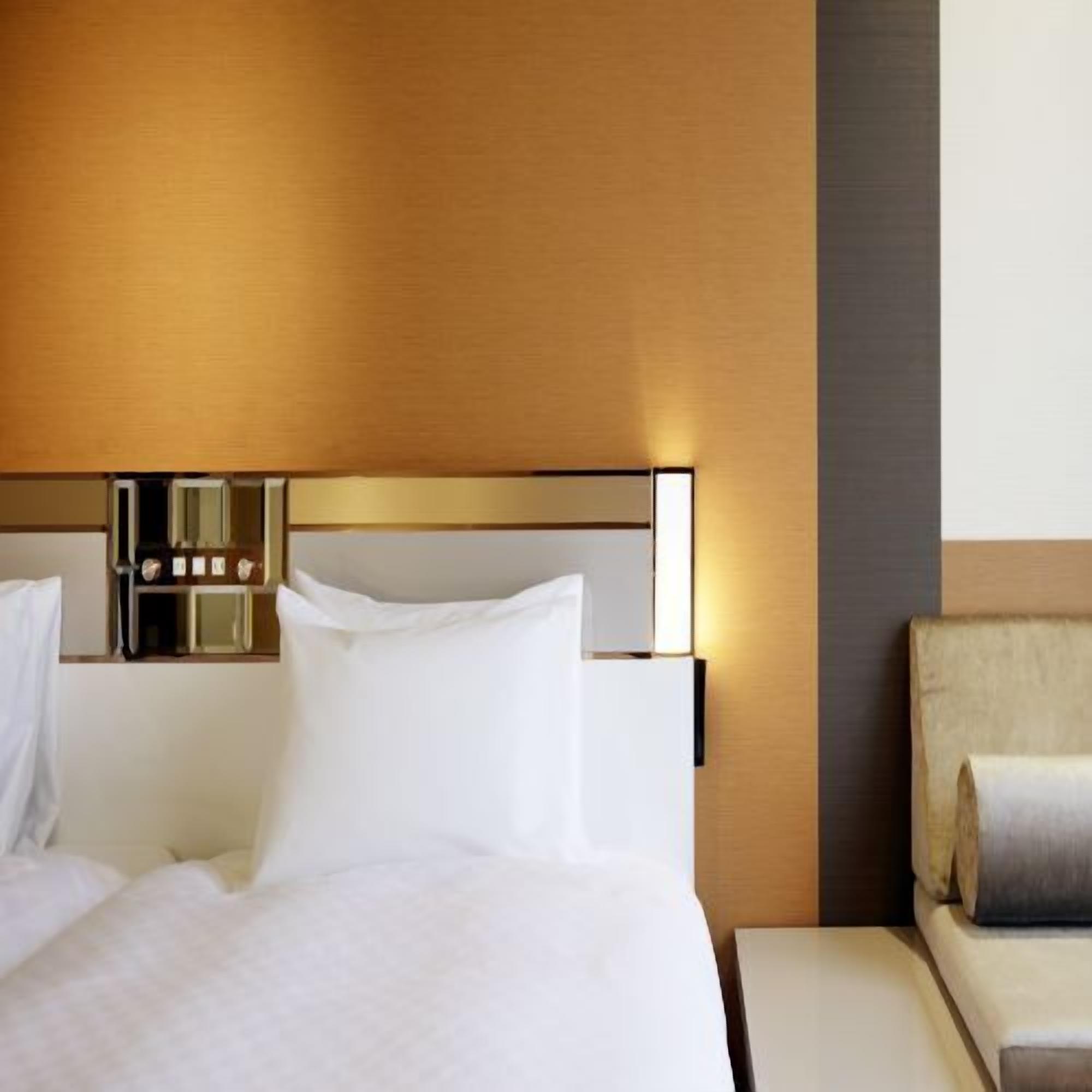 A hotel room with a bed, bedside table, and a chair.