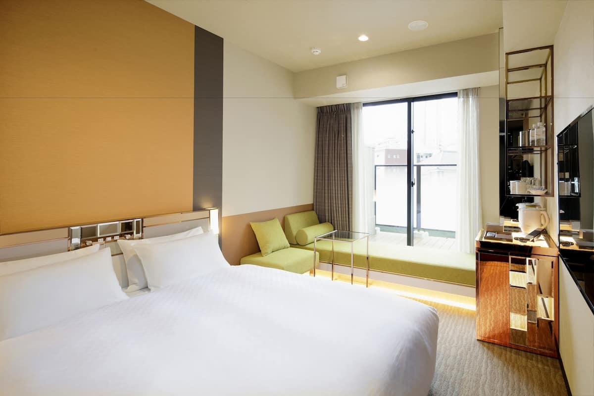 A hotel room with a large bed, a green sofa, a small table, a TV, and a window with curtains.