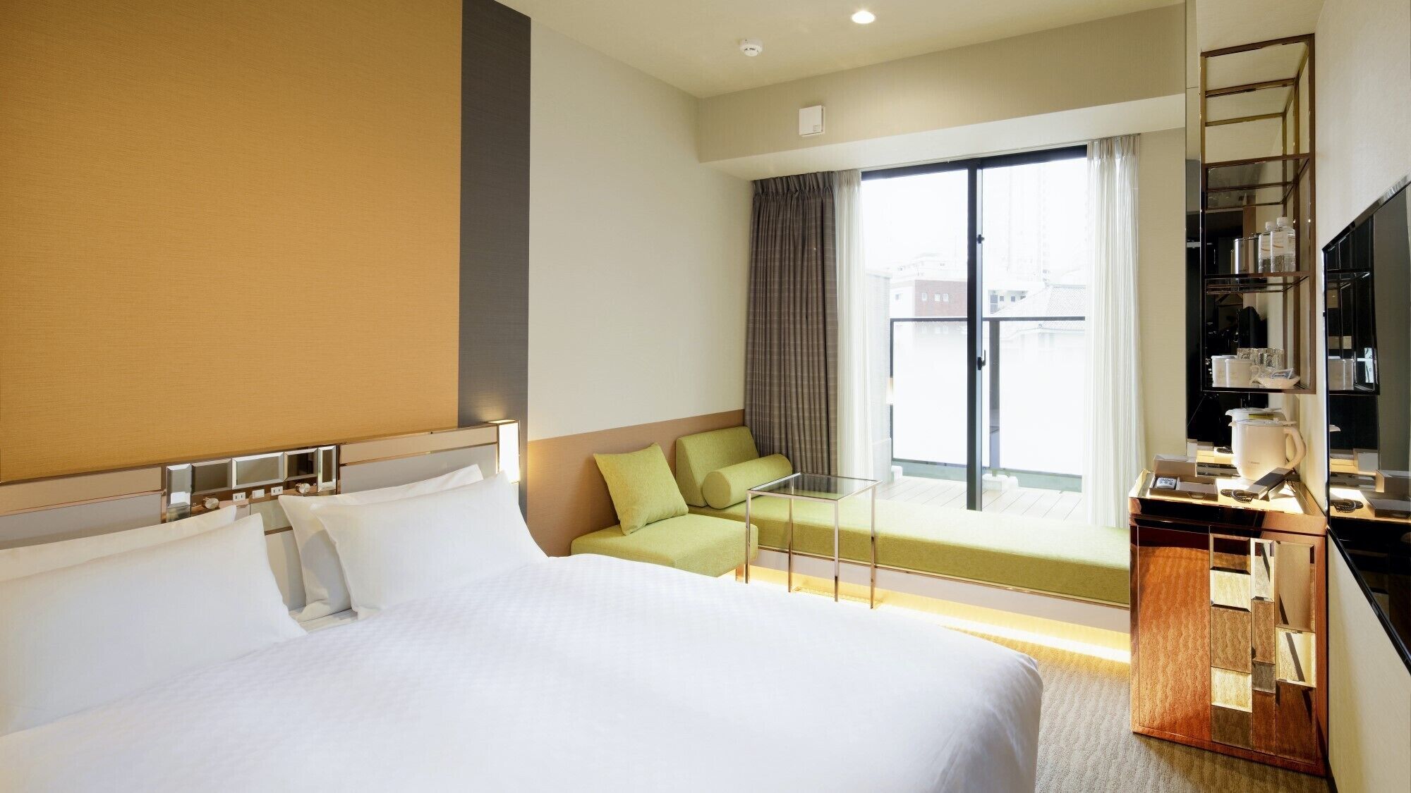 A hotel room with a large bed, a seating area with a glass table, a balcony with curtains, and a minibar.