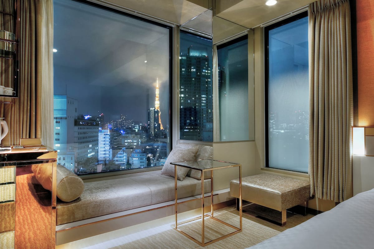 A modern hotel room with a large window offering a city view, a cozy seating area, and a small table.