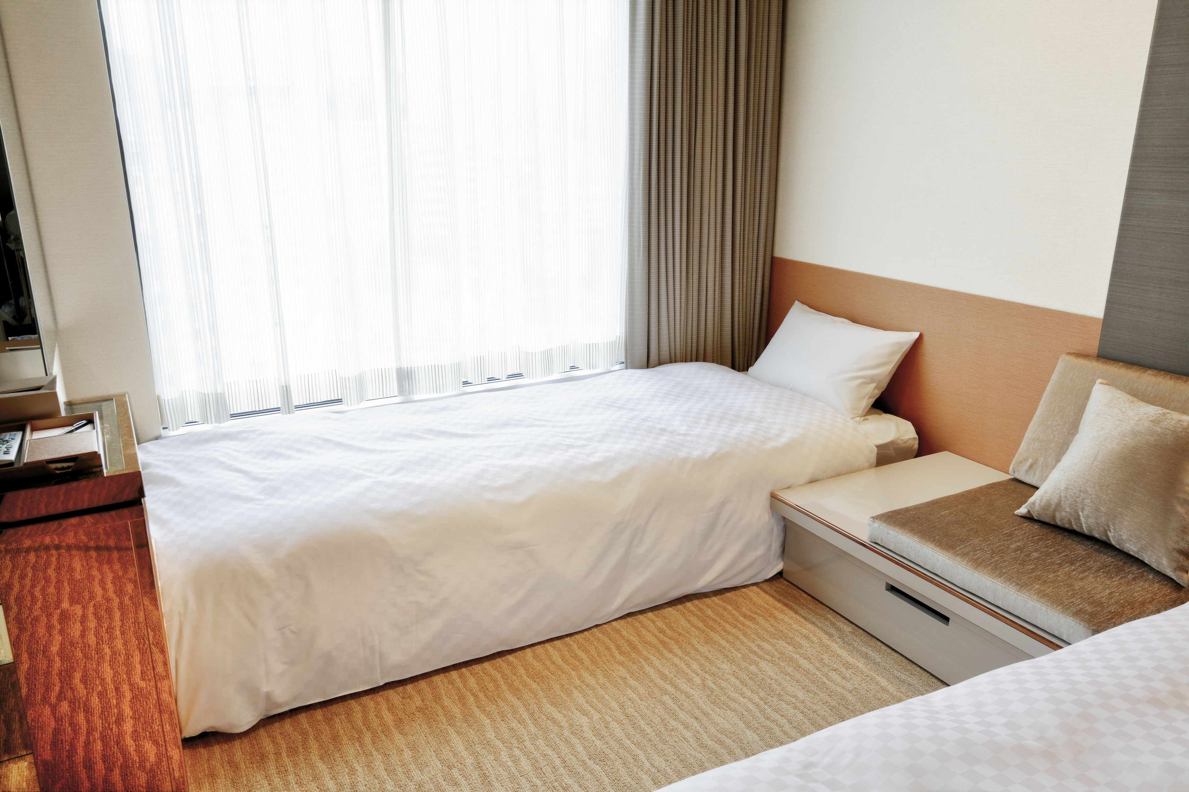 A hotel room with a large bed, a smaller bed, a desk, and a window with curtains.