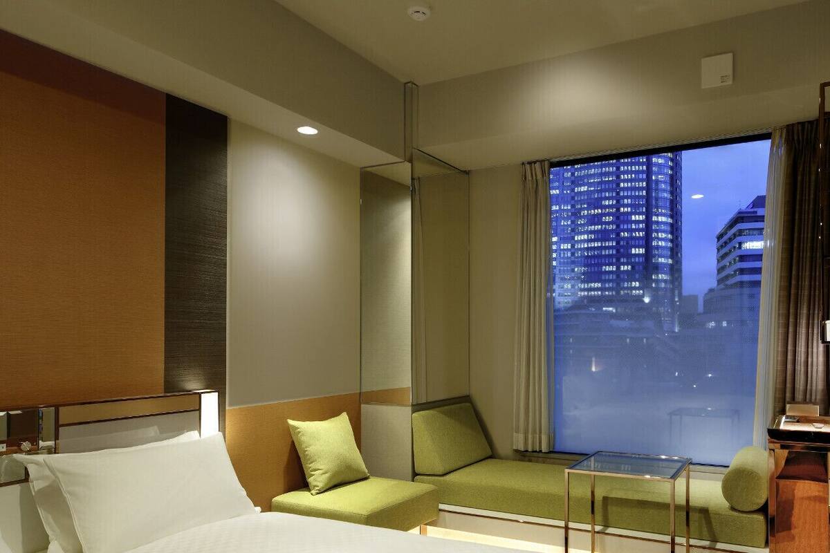 A hotel room with a bed, a green sofa, a small table, and a view of a cityscape at night.
