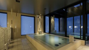 A modern indoor pool area with a glass barrier, marble flooring, and a view of the cityscape at dusk. - Candeo Hotels Tokyo Roppongi (Tokyo)