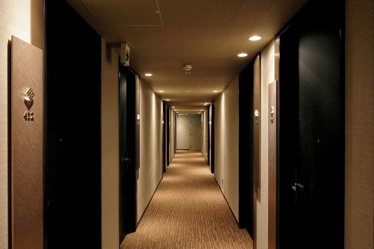 A hotel hallway with carpeted floors, wooden doors, and recessed lighting.