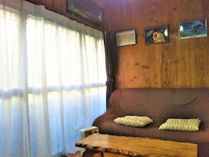 Un interno in legno con un divano marrone, due cuscini, un tavolo di legno e una finestra con tende leggere.