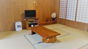 A tatami mat room with a wooden table, a television, and a small cabinet with items on top.