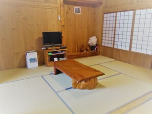 A tatami mat room with a wooden table, a television, and a small cabinet with items on top. - Yakusugi House (Yakushima)