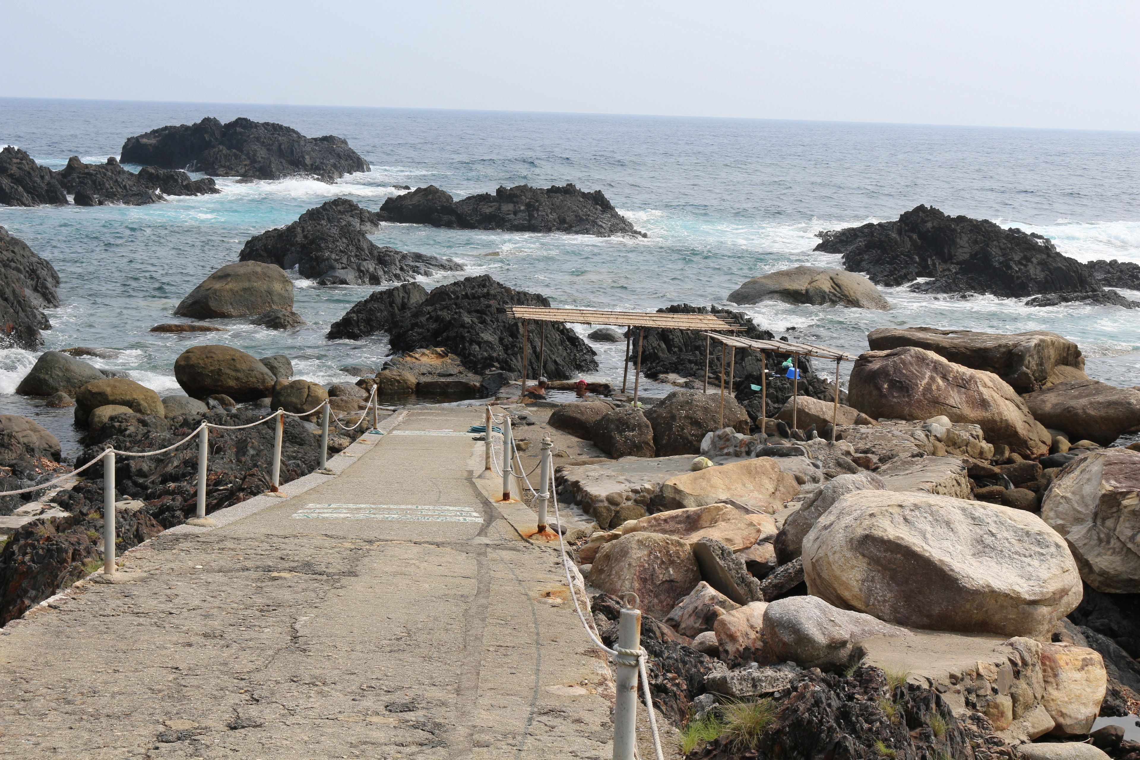 A rocky coastal path leading to a wooden shelter with a view of the ocean.
