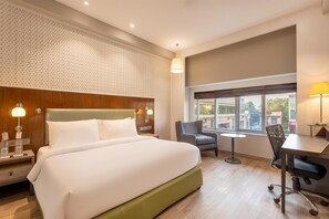 A hotel room with a large bed, a desk, a chair, and a window with a city view. - Country Inn & Suites By Radisson Jammu (Jammu)