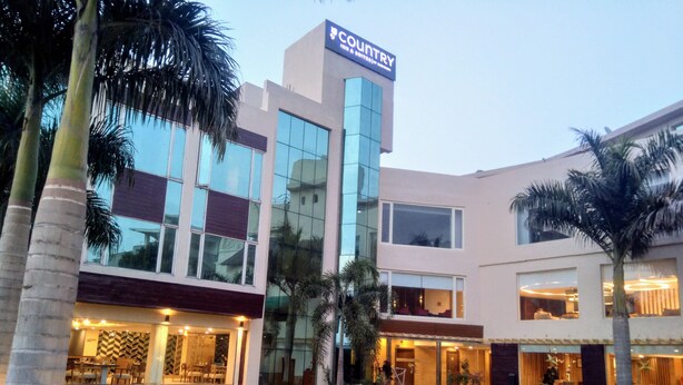 A modern hotel with a glass facade, outdoor seating, and a well-lit entrance. - Country Inn & Suites By Radisson Jammu (Jammu)