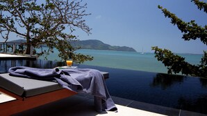 A sun lounger with a towel and a glass of orange juice, overlooking a clear blue sea and distant mountains.
