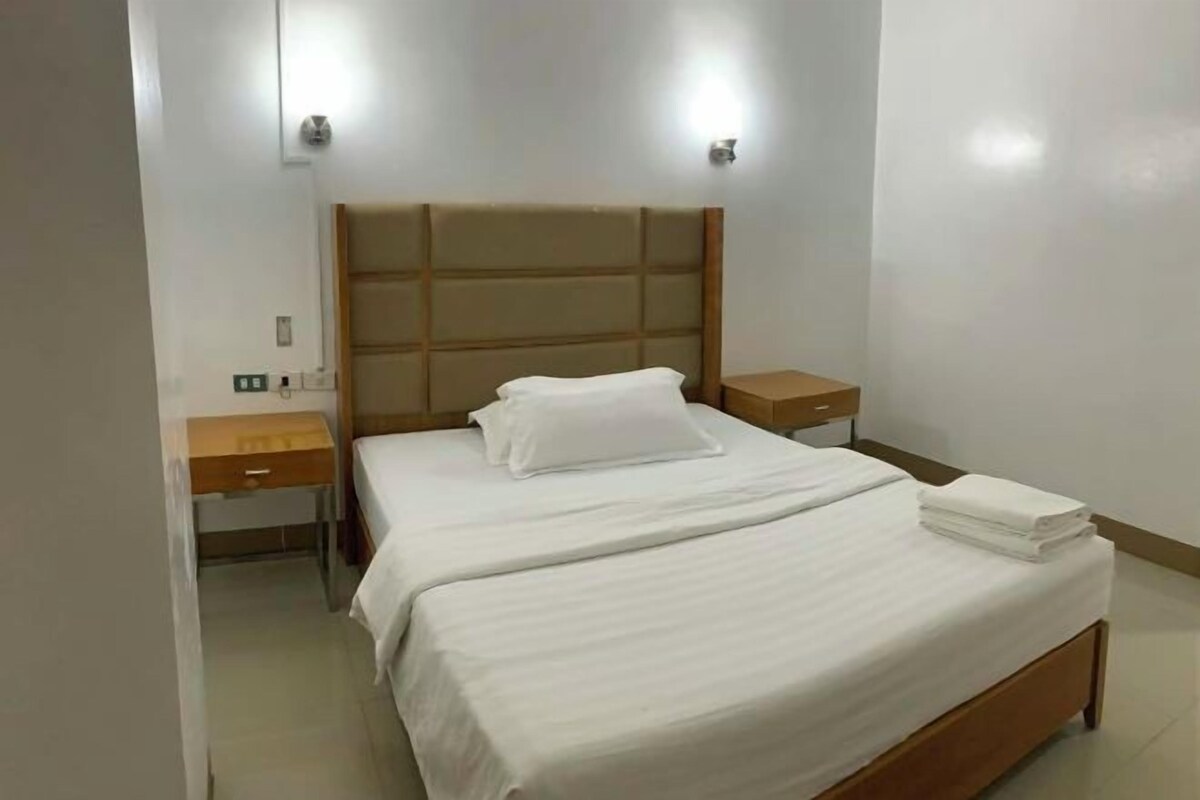 Una cama bien hecha con sábanas blancas, cabecera de madera y dos mesitas de noche con lámparas.