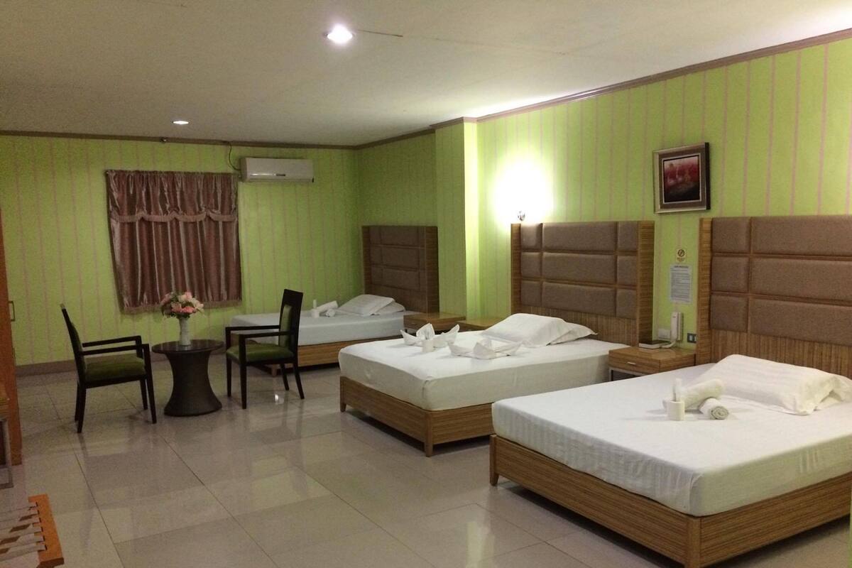 A hotel room with two beds, a desk, chairs, and an air conditioning unit.