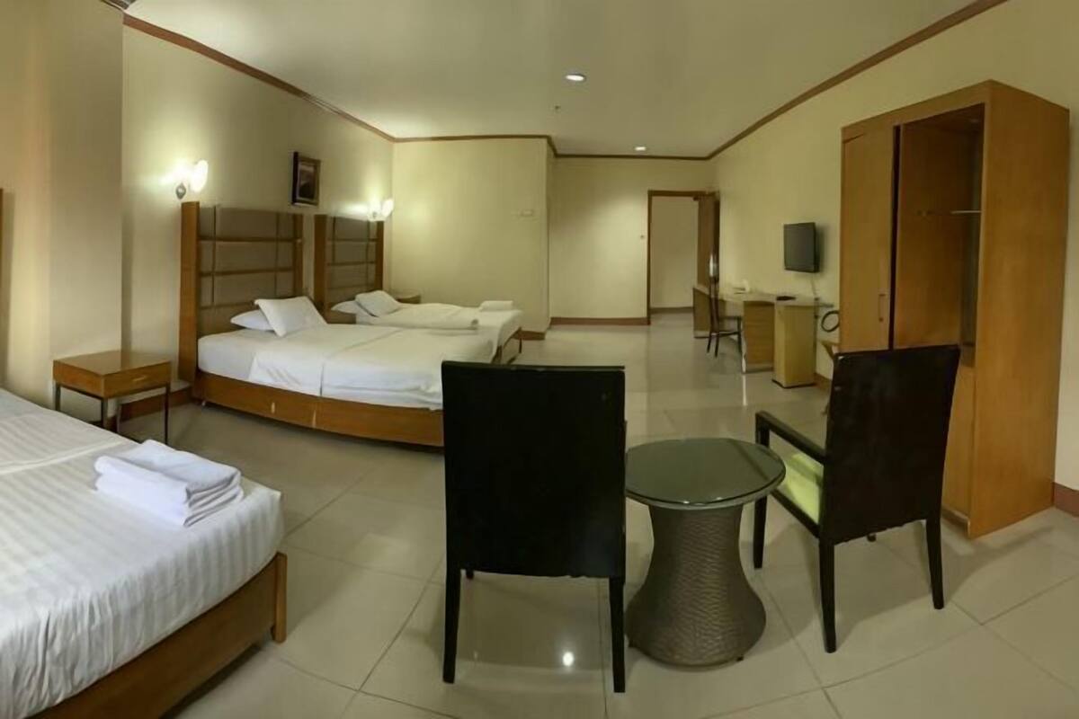 A hotel room with a bed, two chairs, a small table, a TV, and a wardrobe.