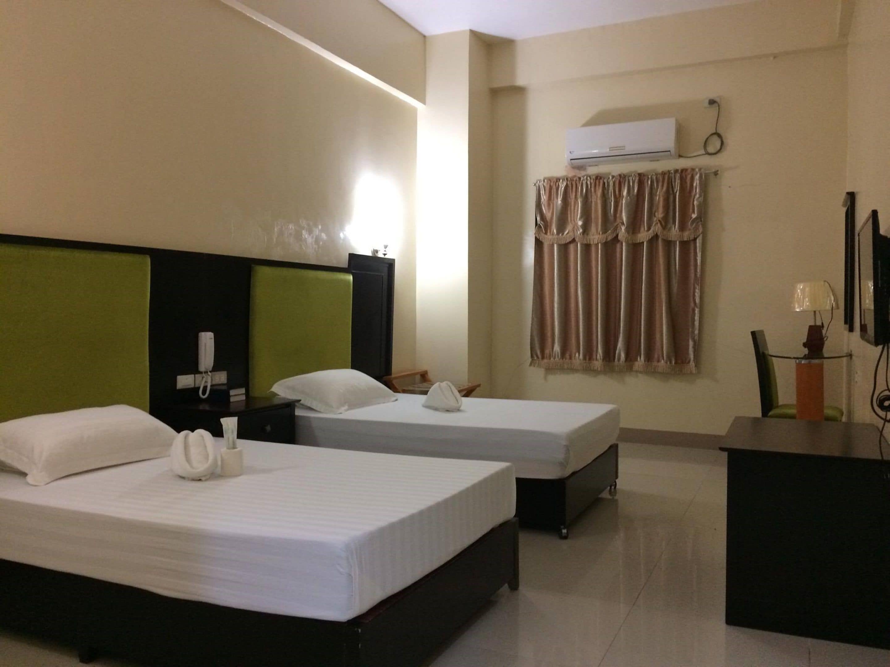 A hotel room with two beds, a desk, a telephone, an air conditioner, and a curtain.