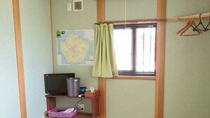 Une pièce avec un sol recouvert de tatamis, un petit tabouret en bois, un téléviseur posé sur une étagère, une carte accrochée au mur et un appareil de climatisation.