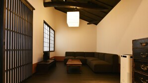 Una habitación con piso de madera, un sofá marrón, una mesita de madera, un televisor sobre un mueble, un calentador y una puerta corredera tradicional.