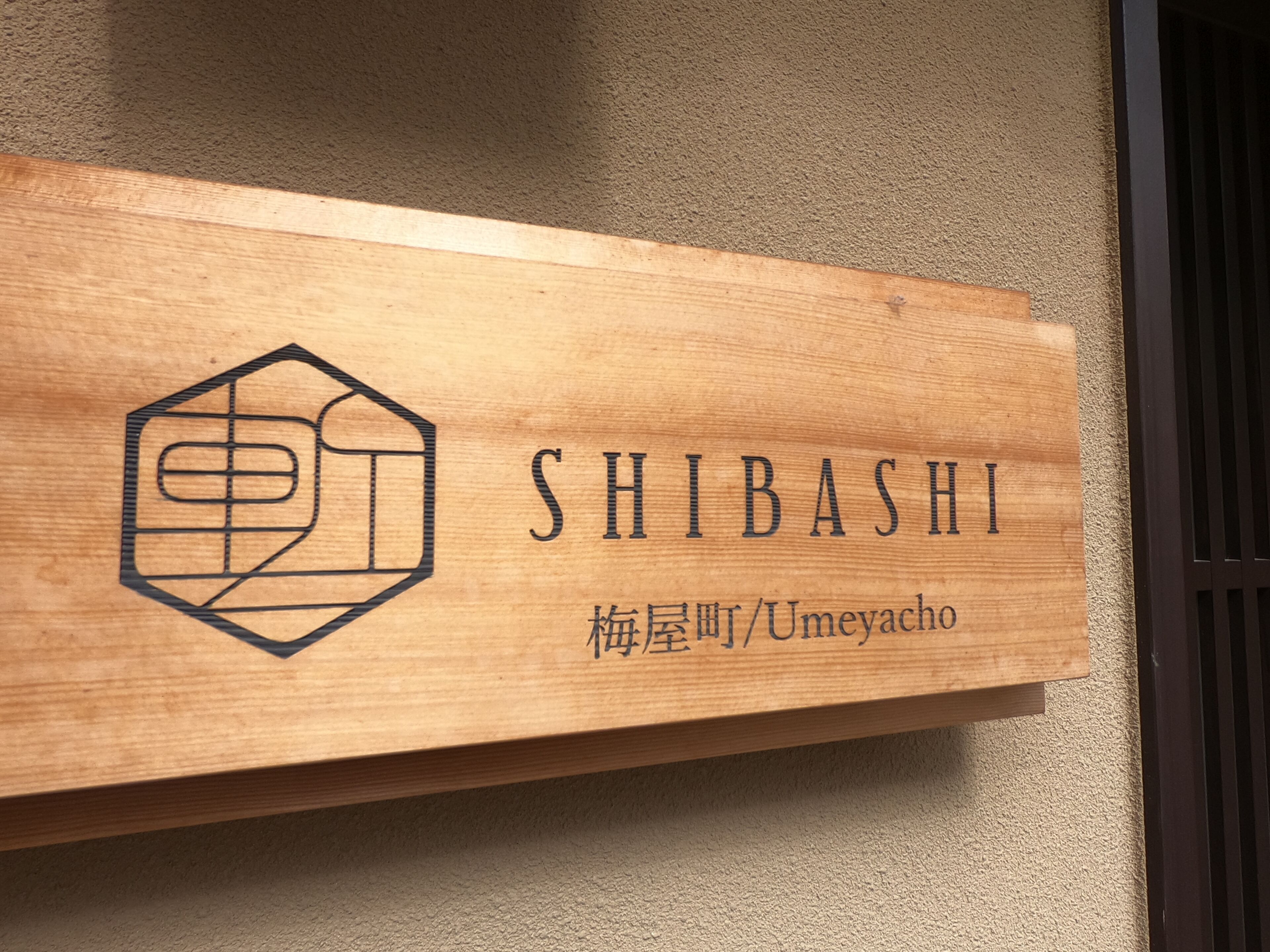 Un letrero de madera con el nombre "SHIBASHI" y una dirección.