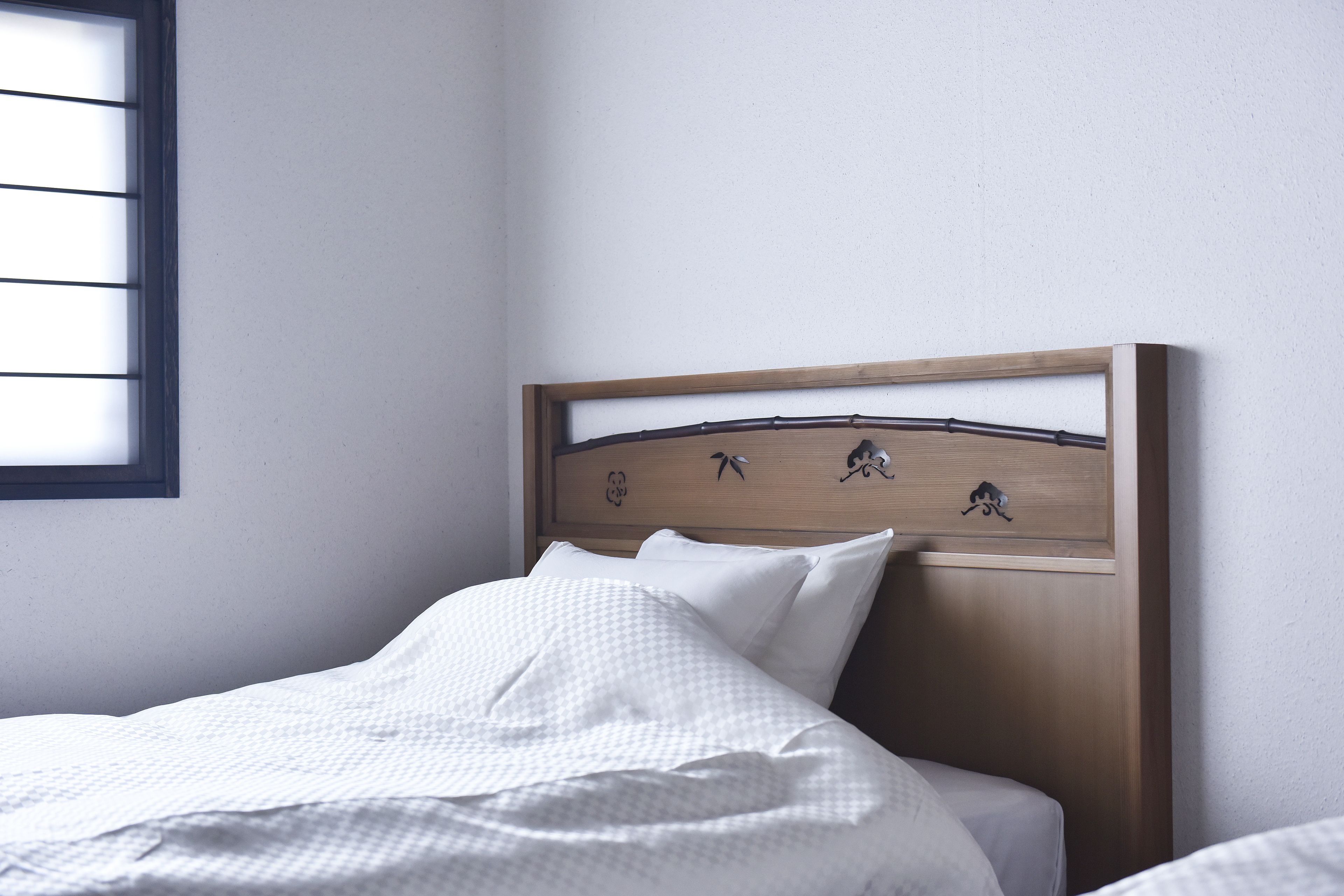 Una cama bien hecha con ropa blanca y cabecera de madera con detalles decorativos.
