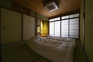 A traditional Japanese room with tatami flooring, a low bed, sliding doors, and a view through shoji screens.
