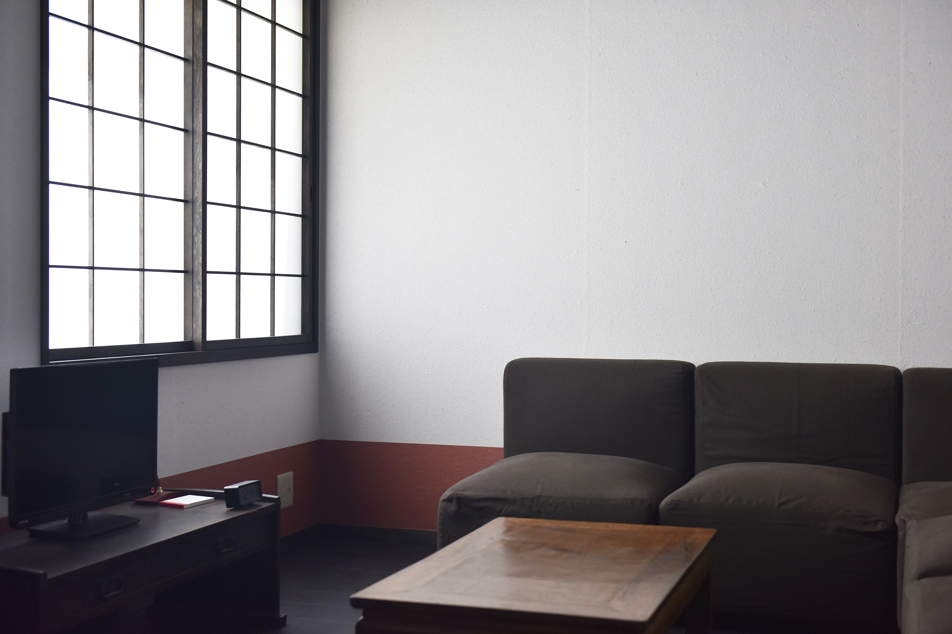 A room with a large window, a dark sofa, a desk with a computer, and a small table.