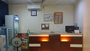 Uma receção com um relógio, um sinal com as tarifas dos quartos e um monitor de computador.
