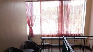 Quarto com varanda, cadeiras de vime, uma mesa e vista para árvores através de cortinas translúcidas.