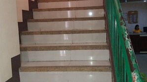 Uma escadaria com degraus brancos e corrimão verde, dando acesso a um andar superior.