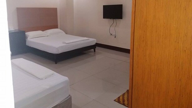 Quarto de hotel com cama, televisão presa à parede e porta de madeira.