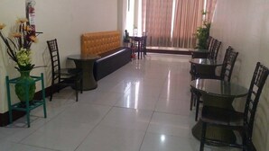 Uma sala de jantar com uma mesa comprida e cadeiras, um banco acolchoado e um vaso com flores.