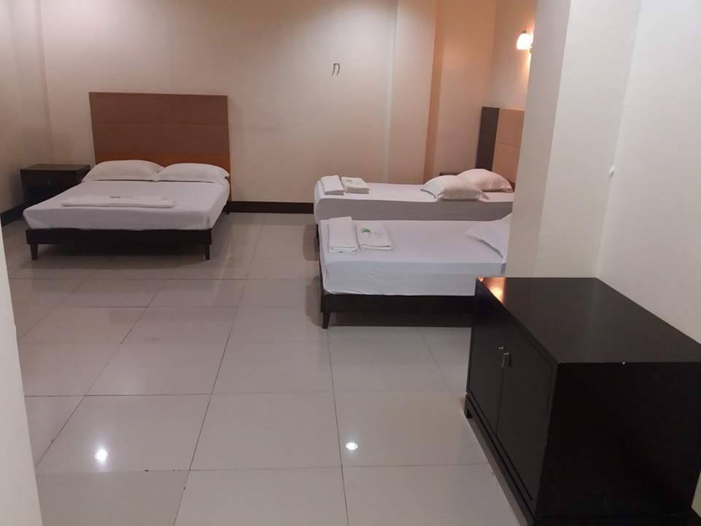 A hotel room with two beds, a dark-colored cabinet, and a tiled floor.