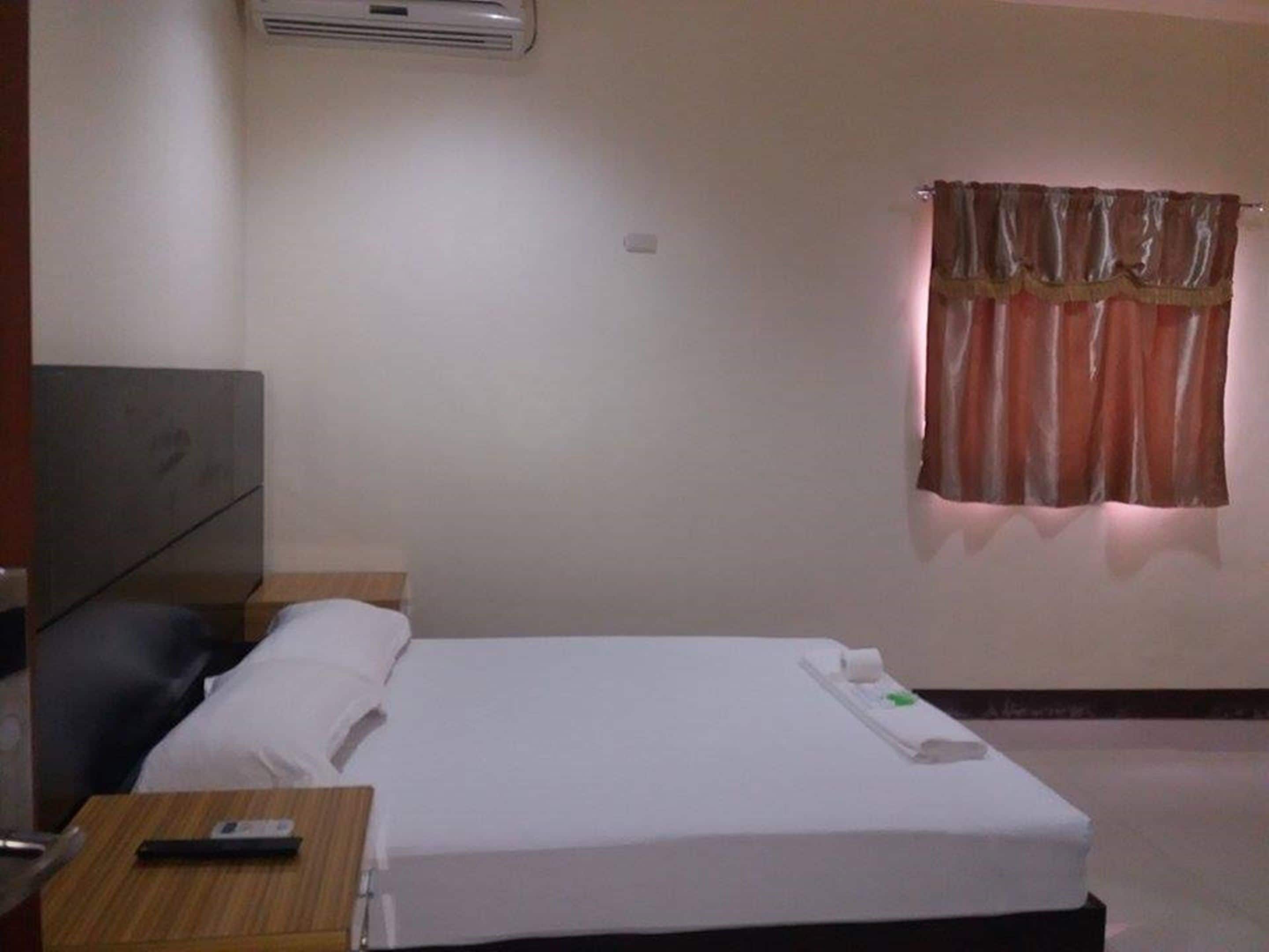 Une chambre d’hôtel avec un lit, une table de chevet, une télécommande et une fenêtre avec des rideaux.