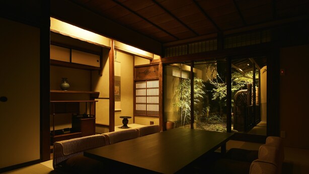 A traditional Japanese room with tatami flooring, a low table, and a view of a garden. - KURAYA Senbonsanjo (Kyoto)
