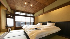 A traditional Japanese-style bedroom with tatami flooring, a large bed with white bedding, and a view through a shoji screen window. - KURAYA Senbonsanjo (Kyoto)