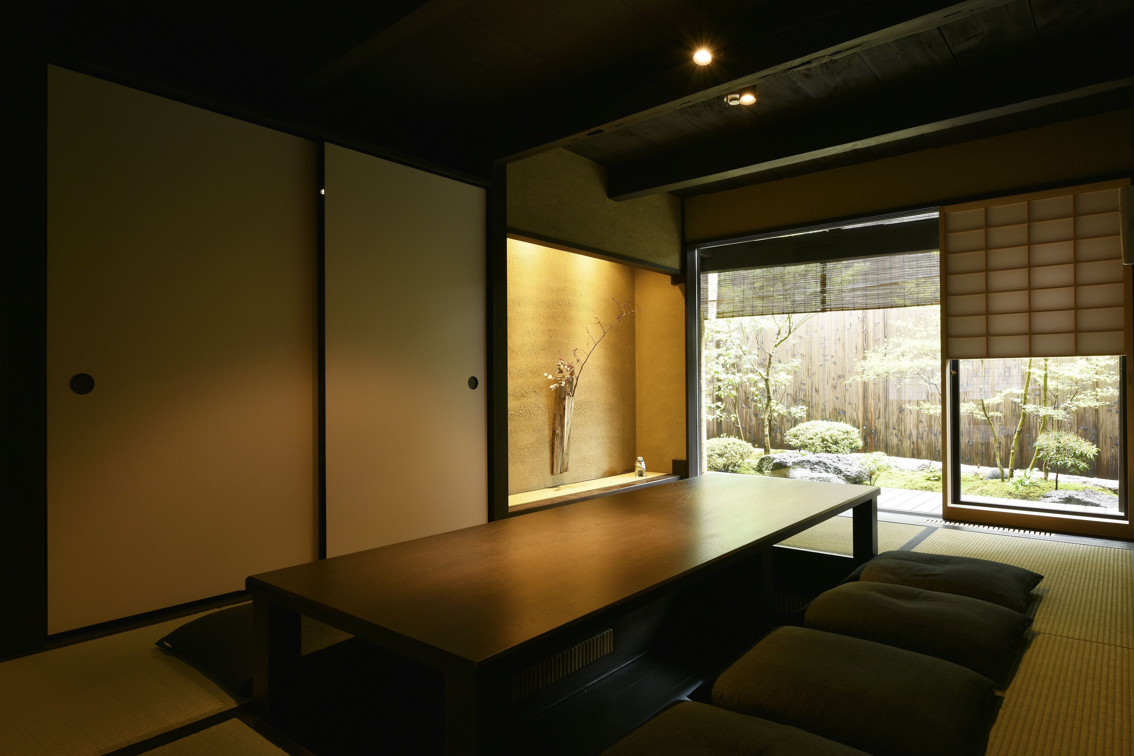 Una habitación japonesa tradicional con suelo de tatami, una mesa baja, puertas correderas y vistas a un jardín.