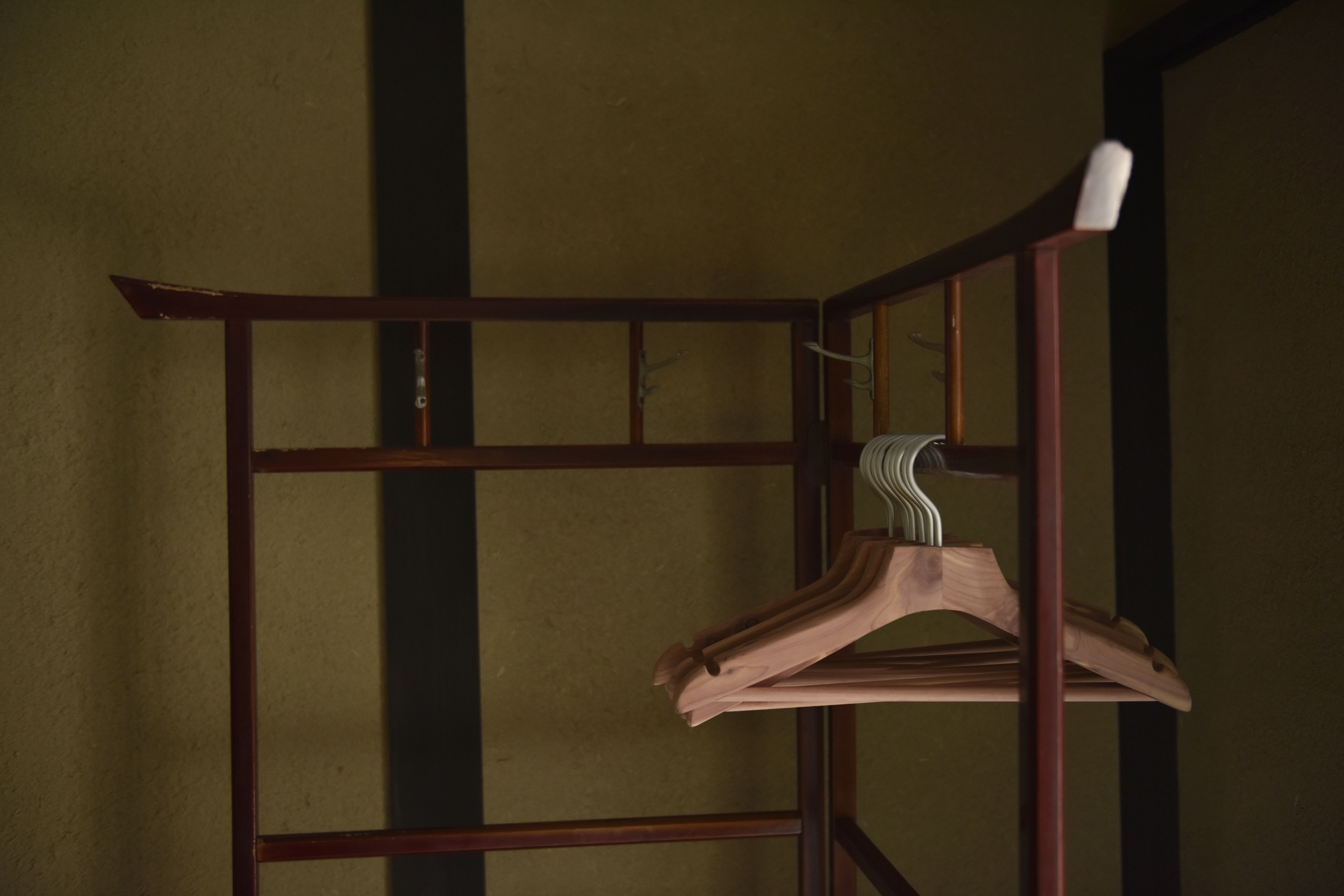 Un cintre en bois, posé sur un porte-manteau en métal, adossé à un mur à texture.