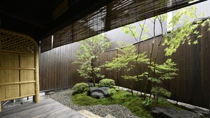 A traditional Japanese garden with a wooden deck, bamboo structures, and a variety of plants and rocks. - KURAYA Nanseicho (Kyoto)