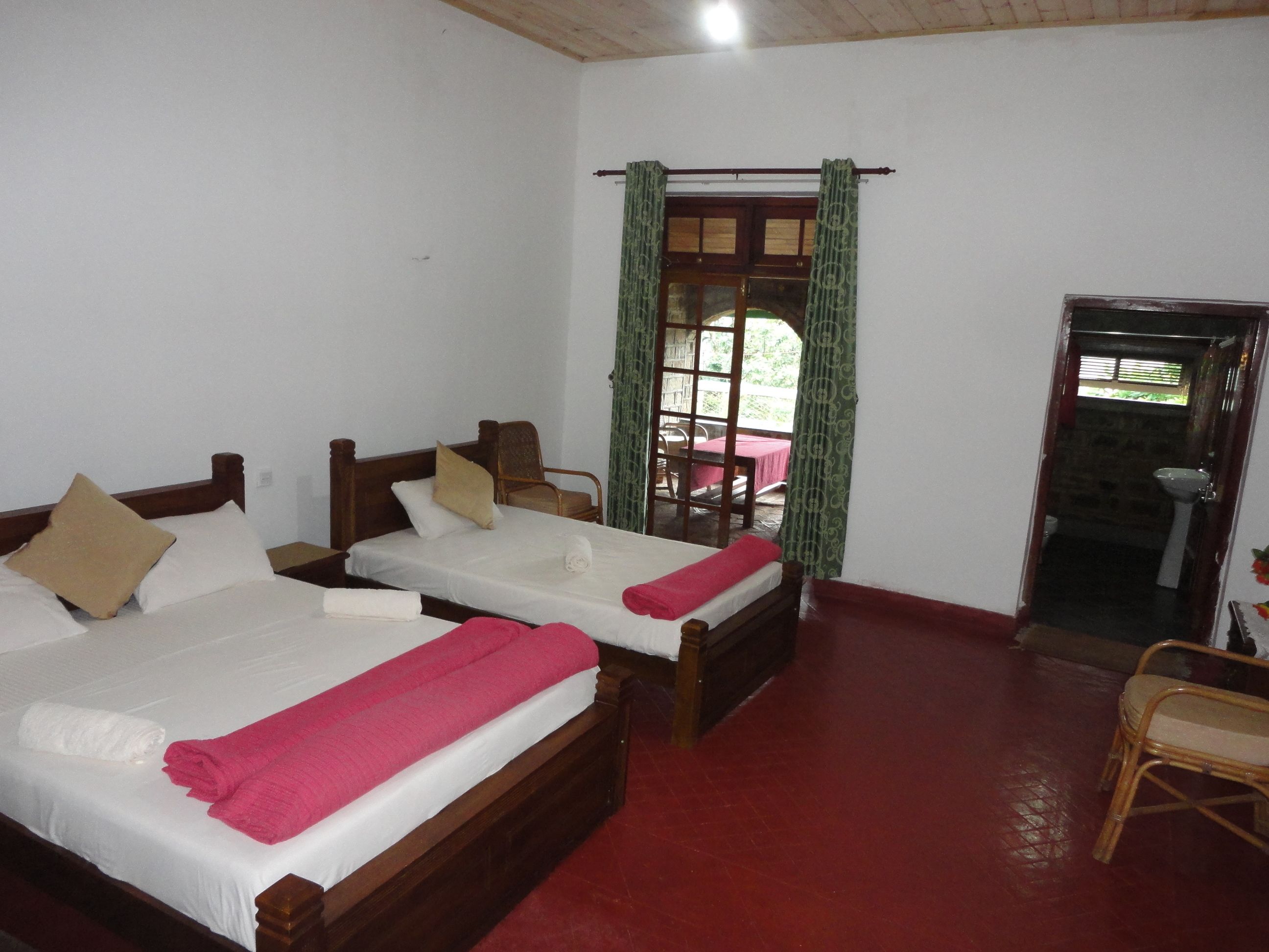 A room with two wooden beds, each with a white mattress and a pink blanket. There is a wooden chair and a small table with a red tablecloth.