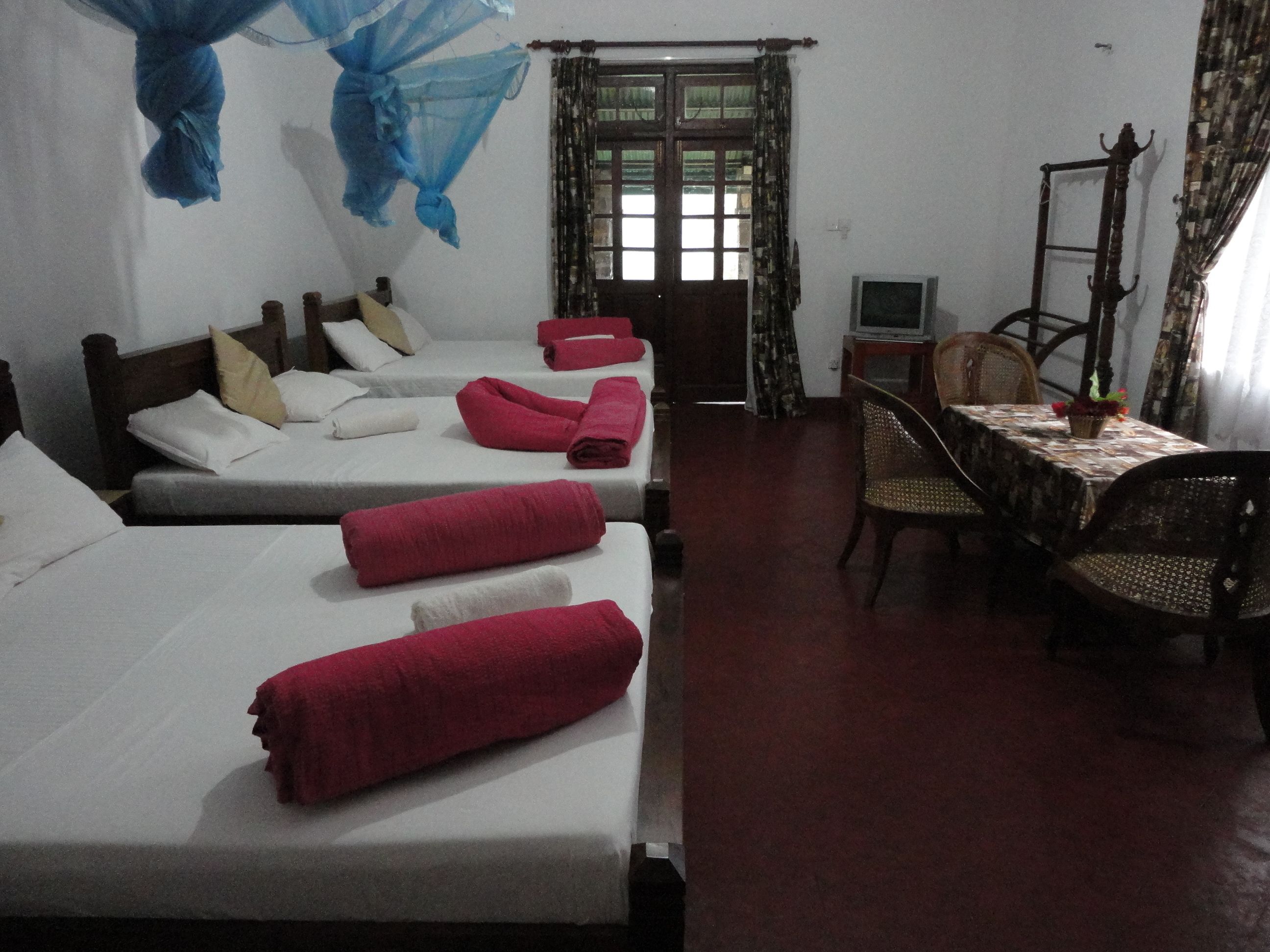 A hotel room with four beds, a small table with a TV, and a chair.