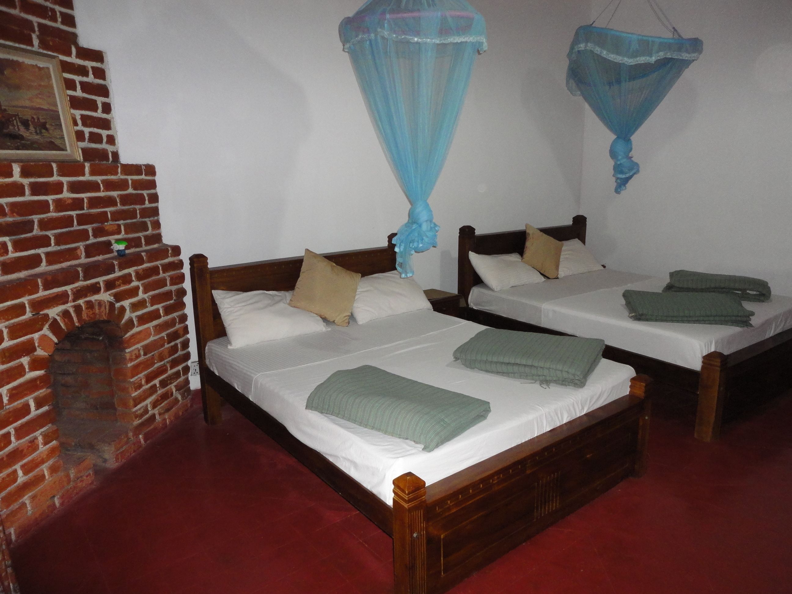 A room with two wooden beds, a brick fireplace, and mosquito nets hanging from the ceiling.
