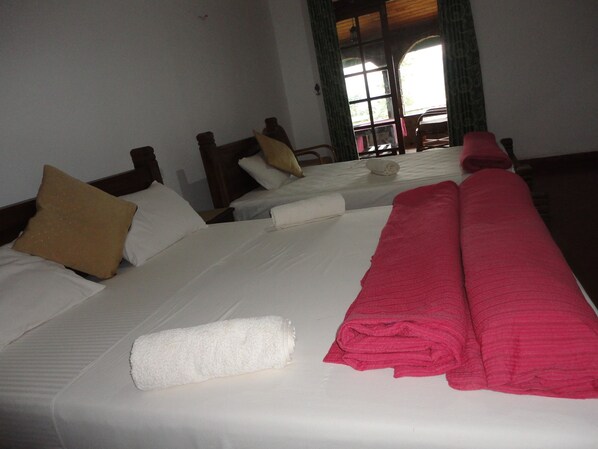 A hotel room with three beds, each with white linens and pillows. There are rolled towels on the beds.