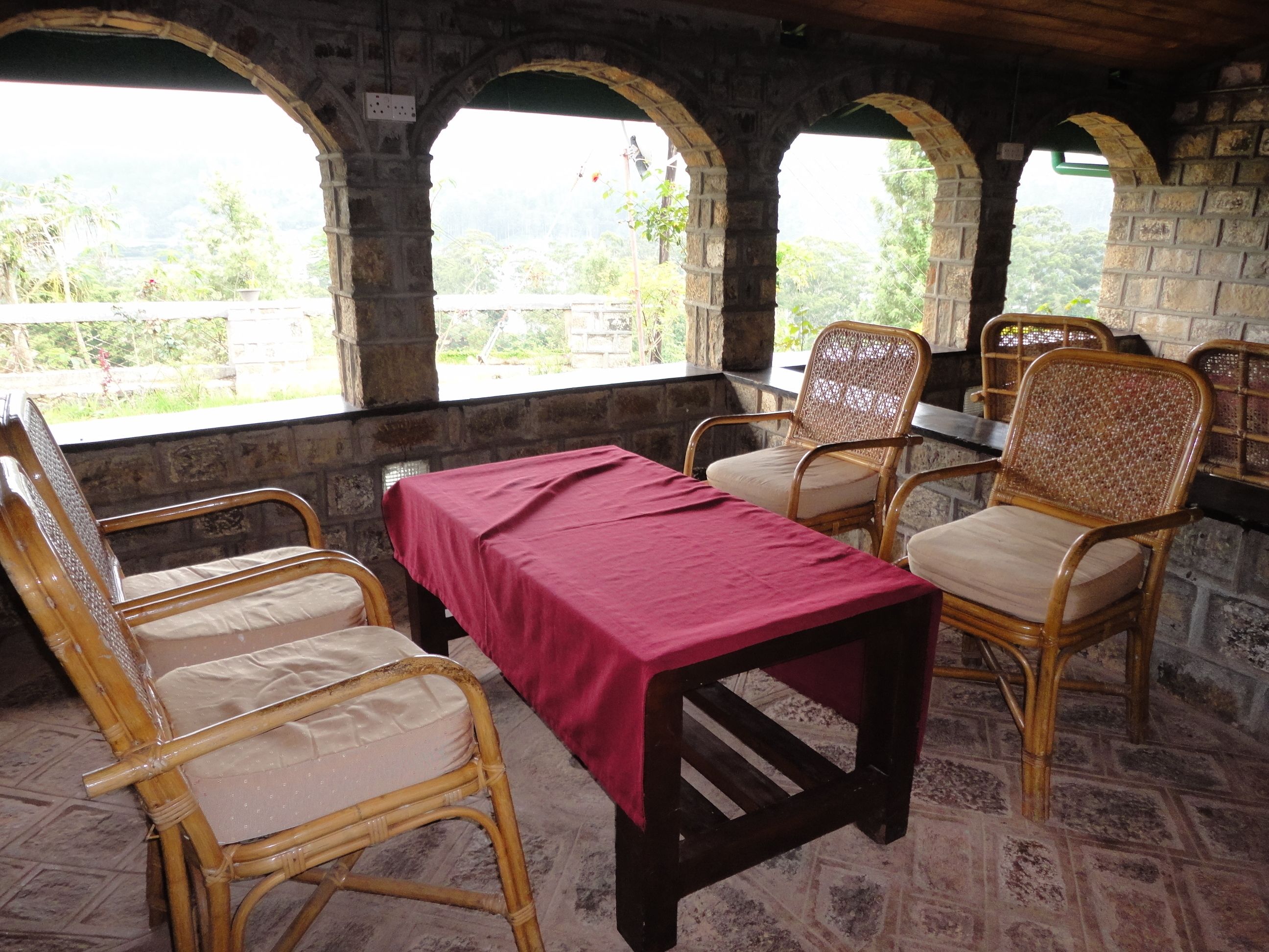 A covered outdoor seating area with stone arches, a table with a red tablecloth, and wicker chairs.