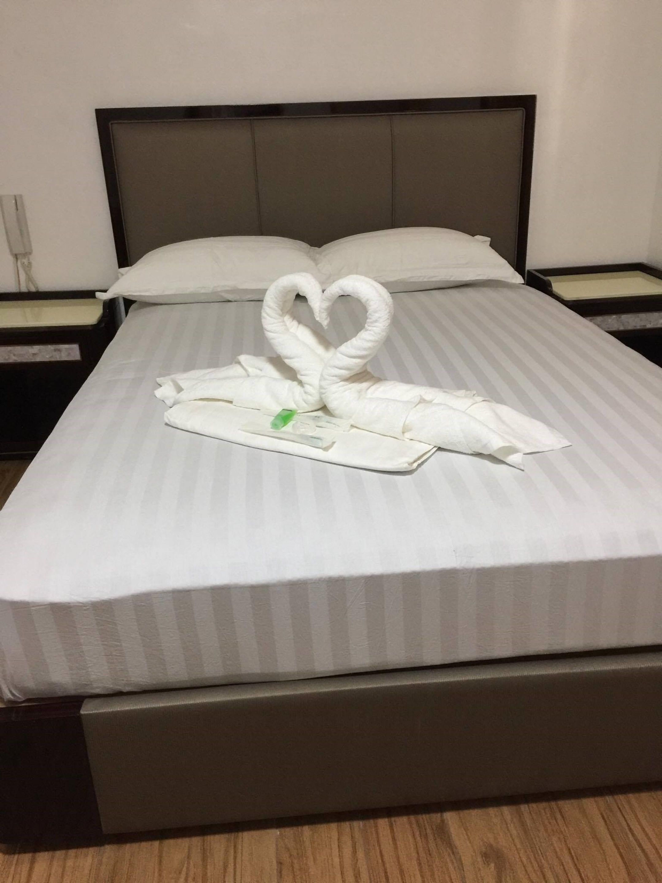 A hotel room with a bed featuring a heart-shaped towel arrangement.