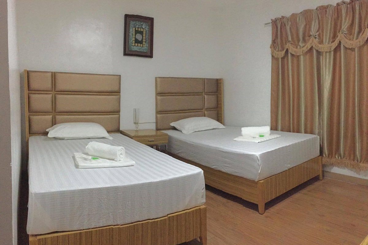 A hotel room with two beds, each with a headboard, a bedside table, and a framed picture on the wall.